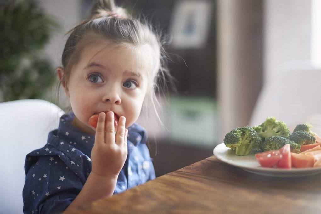 little girl putting a slice of tomato into her mouth during a meal