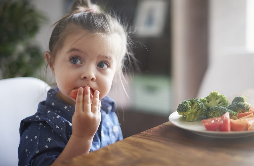 little girl putting a slice of tomato into her mouth during a meal