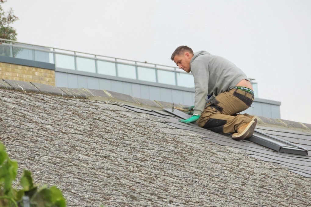man installing shingles on a sloped roof under cloudy skies