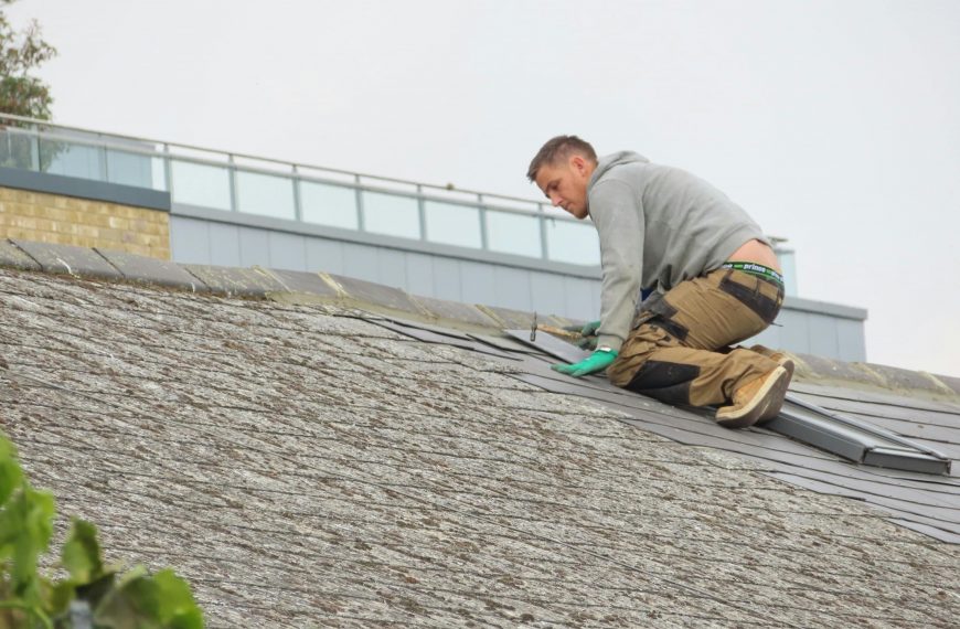 man installing shingles on a sloped roof under cloudy skies